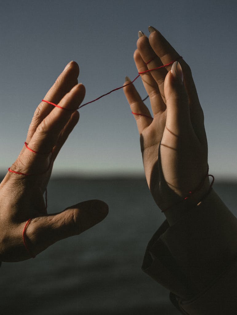 Two hands connected by a red string symbolizing fate and connection.